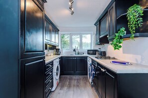 A kitchen with black cabinets, a washing machine, a microwave, and a hanging plant. - Huge 4BR House | Driveway | Pool Table (Birkby)