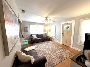 Ein Wohnzimmer mit einer Couch, einem gemusterten Teppich, einem Deckenventilator und einer Tür.