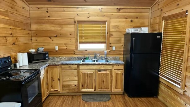 A wooden cabin kitchen with a stove, microwave, sink, and black refrigerator. - Cozy Cabin #2 Near Lake Merrisach in Tichnor AR (Tichnor)
