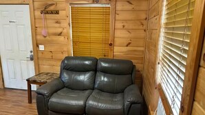 A wooden cabin interior with a black leather sofa, a small wooden table, and a door with a 'No Smoking' sign. - Cozy Cabin #2 Near Lake Merrisach in Tichnor AR (Tichnor)