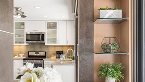 Una cocina moderna con armarios blancos, microondas, estufa y una repisa de vidrio con plantas.