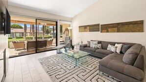 Una sala moderna con una mesa de centro de vidrio, un sofá y vistas a un patio con mobiliario exterior.