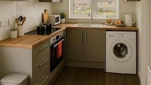Een compacte keuken met een ingebouwde wasmachine, houten aanrechtblad en een raam dat voor daglicht zorgt.