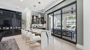 Une cuisine moderne dotée d’un grand îlot central, d’un coin repas avec des chaises blanches et d’une vue sur l’espace piscine grâce à de grandes portes coulissantes.