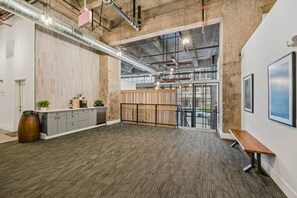 Ein offenes Büro mit hoher Decke, freiliegenden Lüftungsrohren, einer Holzbank, einer Theke mit Pflanzen und Blick durch große Fenster.