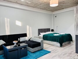 Un dormitorio moderno con una cama, un sofá, una mesita de centro y una mesita auxiliar.