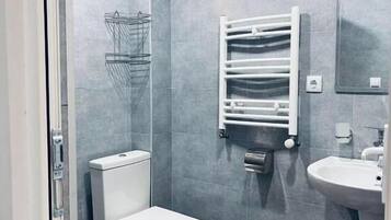 Un baño con azulejos grises, un inodoro, un lavamanos, un perchero para toallas y una ducha.