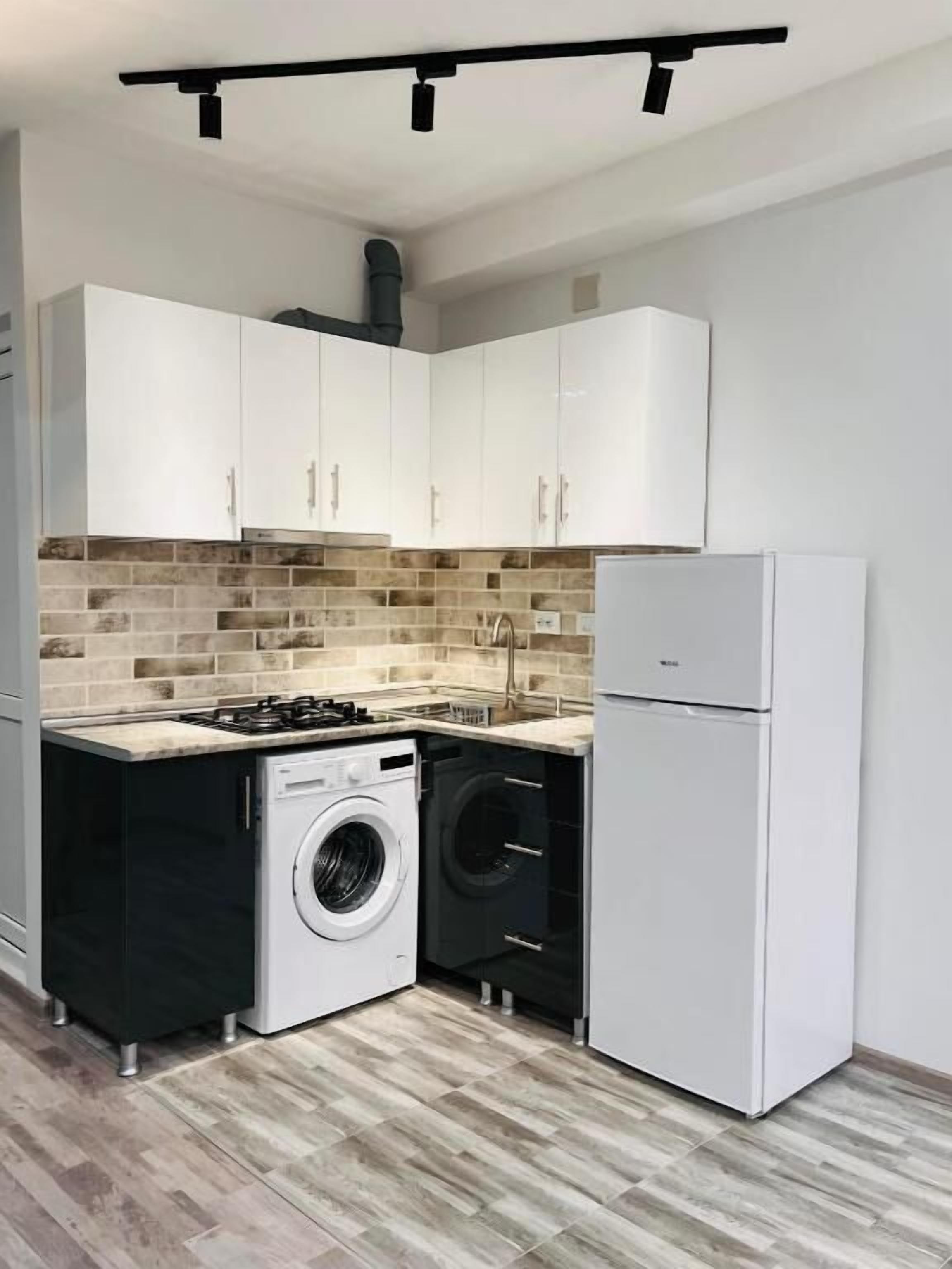 Cocina compacta con armarios blancos, lavadora, refrigerador y estufa a gas.