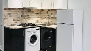 Cocina compacta con armarios blancos, lavadora, refrigerador y estufa a gas.