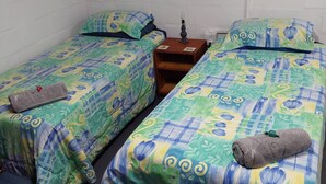 A room with two single beds, each with a patterned bedspread, a nightstand with a lamp, and a small wooden cabinet.