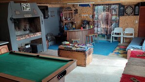 A pool table, a barbecue grill, and a dartboard in a room with wooden beams and a colorful mural.