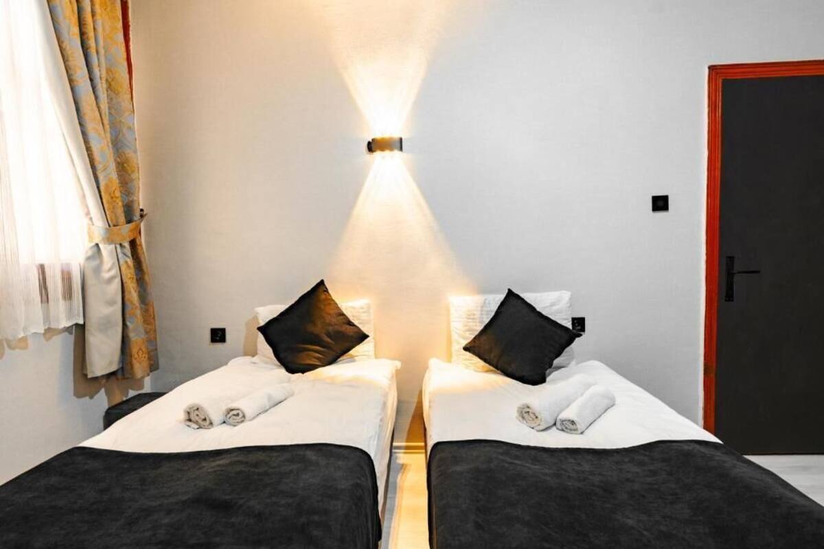 Una habitación con dos camas, una lámpara en la pared, una puerta y una ventana con cortinas.