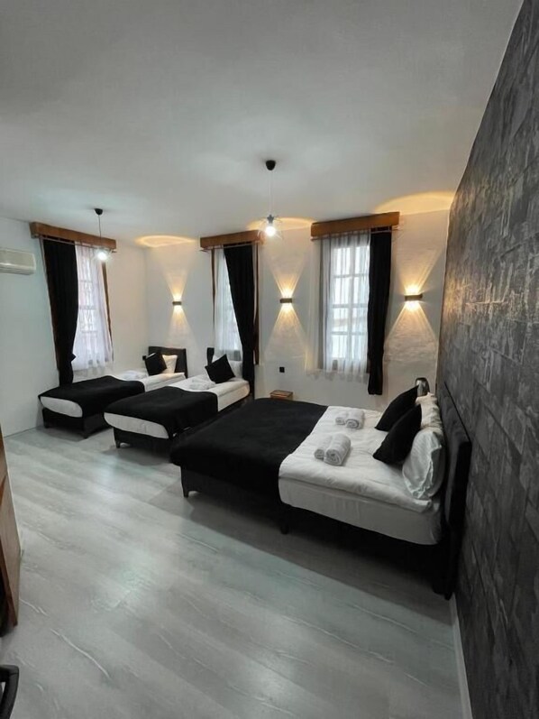 Habitación de hotel con tres camas, un espejo grande y una pared de detalles de piedra.