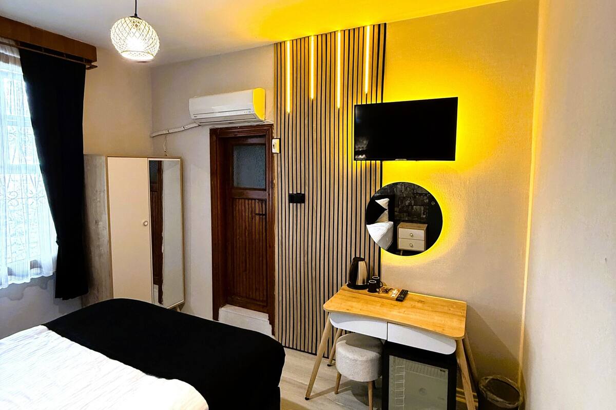 Una habitación de hotel con cama, escritorio con espejo, televisión y ventana con cortinas.