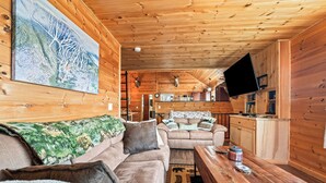 Interior de una cabaña de madera con sofá, mesa de centro y televisor montado.
