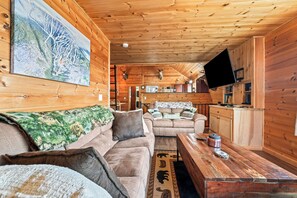 Ein Interieur einer Holzhütte mit einer Couch, einem Couchtisch und einem Wandfernseher.