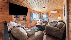 Interior de una cabaña de madera con sofá, sillón y televisión de pantalla plana.