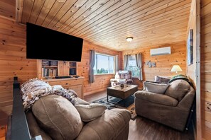 Ein Holzblockhaus-Innenraum mit einer Couch, einem Sessel und einem Flachbildfernseher.