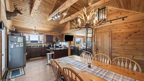 Interior de una cabaña de madera con una mesa de comedor, sillas, una zona de cocina y trofeos de animales colgados.