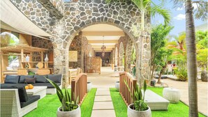 A stone archway leading to a lounge area with sofas, potted plants, and a view of the interior.