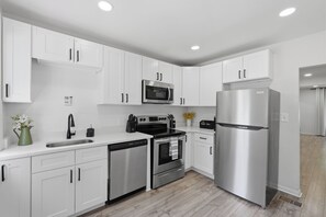 A modern kitchen with white cabinets, stainless steel appliances, a dishwasher, and a sink.