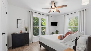 Ein Schlafzimmer mit einem Bett, einem Deckenventilator, einem Fernseher und einem Fenster mit Vorhängen.