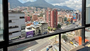 Vista de la ciudad desde una ventana, con edificios, una carretera y montañas al fondo.