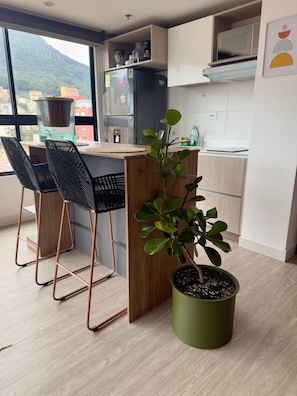 Eine moderne Küche mit einer Holzinsel, zwei schwarzen Stühlen, einem Topf mit Pflanze und Blick auf Gebäude durch große Fenster.