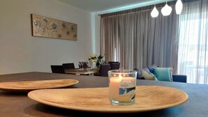 Une table à manger avec deux sets de table ronds en bois, une bougie allumée, et un coin repas avec un canapé et des rideaux en arrière-plan.