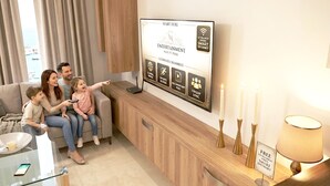 Une famille se trouve dans un salon moderne, avec un téléviseur fixé au mur qui affiche différentes options de divertissement, une table basse en verre et une console en bois au design minimaliste.