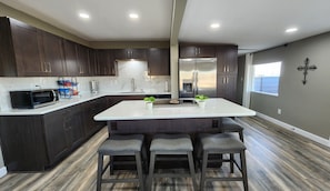 Una cocina moderna con armarios de madera oscura, una isla blanca con taburetes de bar, un refrigerador de acero inoxidable y una cruz en la pared.