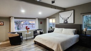 Une chambre à coucher avec un grand lit, un bureau, une chaise, une fenêtre donnant sur un beau paysage et un luminaire au plafond.