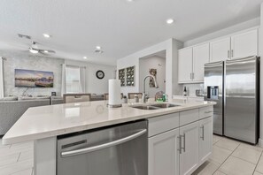 Eine moderne Küche mit einem Edelstahl-Kühlschrank, einem eingebauten Geschirrspüler und einer großen Kochinsel mit Spüle.