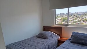 A bedroom with two beds, a wooden headboard, and a window with a city view.
