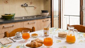 Aamiaispöytä, jossa on croissantteja, appelsiinimehua ja kannullinen mehua, ja pöydällä on kukkakuviollinen pöytäliina.