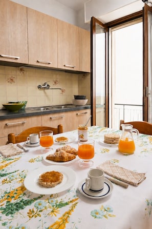 Colazione con croissant, succo d'arancia e una brocca di succo su un tavolo con una tovaglia floreale.