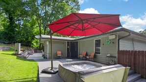 A backyard with a hot tub, patio chairs, a red umbrella, and a wooden deck. - Modern East ATL Holiday Getaway (Atlanta)