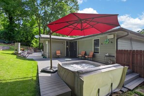 Ein Garten mit Whirlpool, Terrassenstühlen, einem roten Sonnenschirm und einer Holzterrasse.