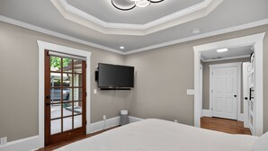 A bedroom with a large bed, a mounted TV, and a door leading to a balcony. - Modern East ATL Holiday Getaway (Atlanta)