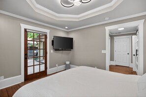 Ein Schlafzimmer mit einem großen Bett, einem an der Wand befestigten Fernseher und einer Tür, die auf einen Balkon führt.