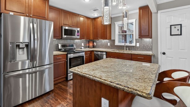A modern kitchen with stainless steel appliances, wooden cabinets, granite countertops, and pendant lighting. - Modern East ATL Holiday Getaway (Atlanta)