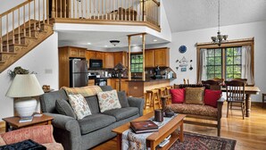 Amplia sala de estar con escalera, muebles de madera y una cocina al fondo.