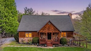 Una cabaña de troncos con cimientos de piedra, un porche y una chimenea de piedra.