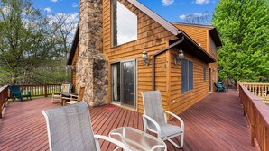 Una cabaña de madera con terraza, pared de piedra y asientos exteriores.