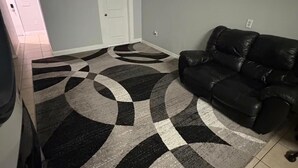 Una sala de estar con un sofá de cuero negro, una alfombra estampada y una puerta blanca.