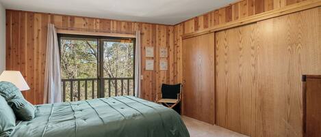 Una habitación con paneles de madera, un ventanal grande, una cama con ropa de cama verde, una silla y una lámpara.