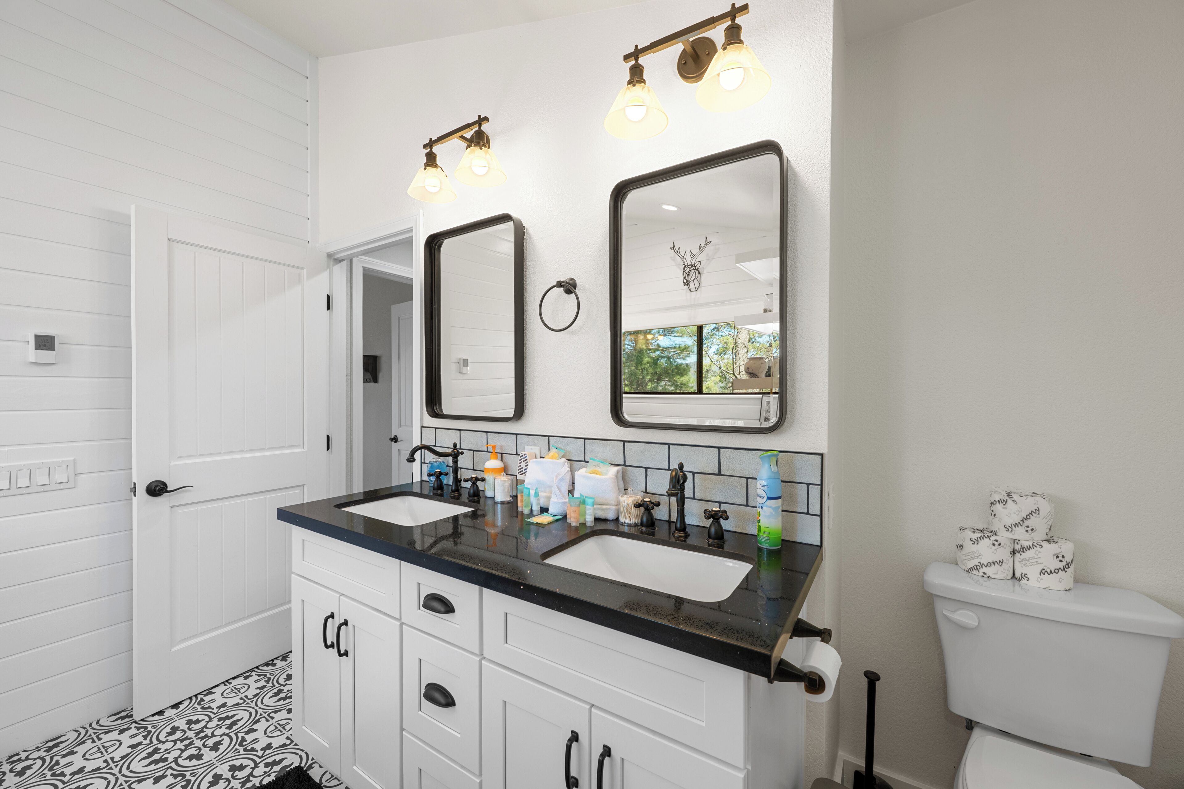 A bathroom with two sinks, a toilet, and a mirror with lights above.