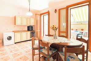 Una cocina con lavadora, armarios de madera, una mesa de comedor con sillas y un florero con flores.