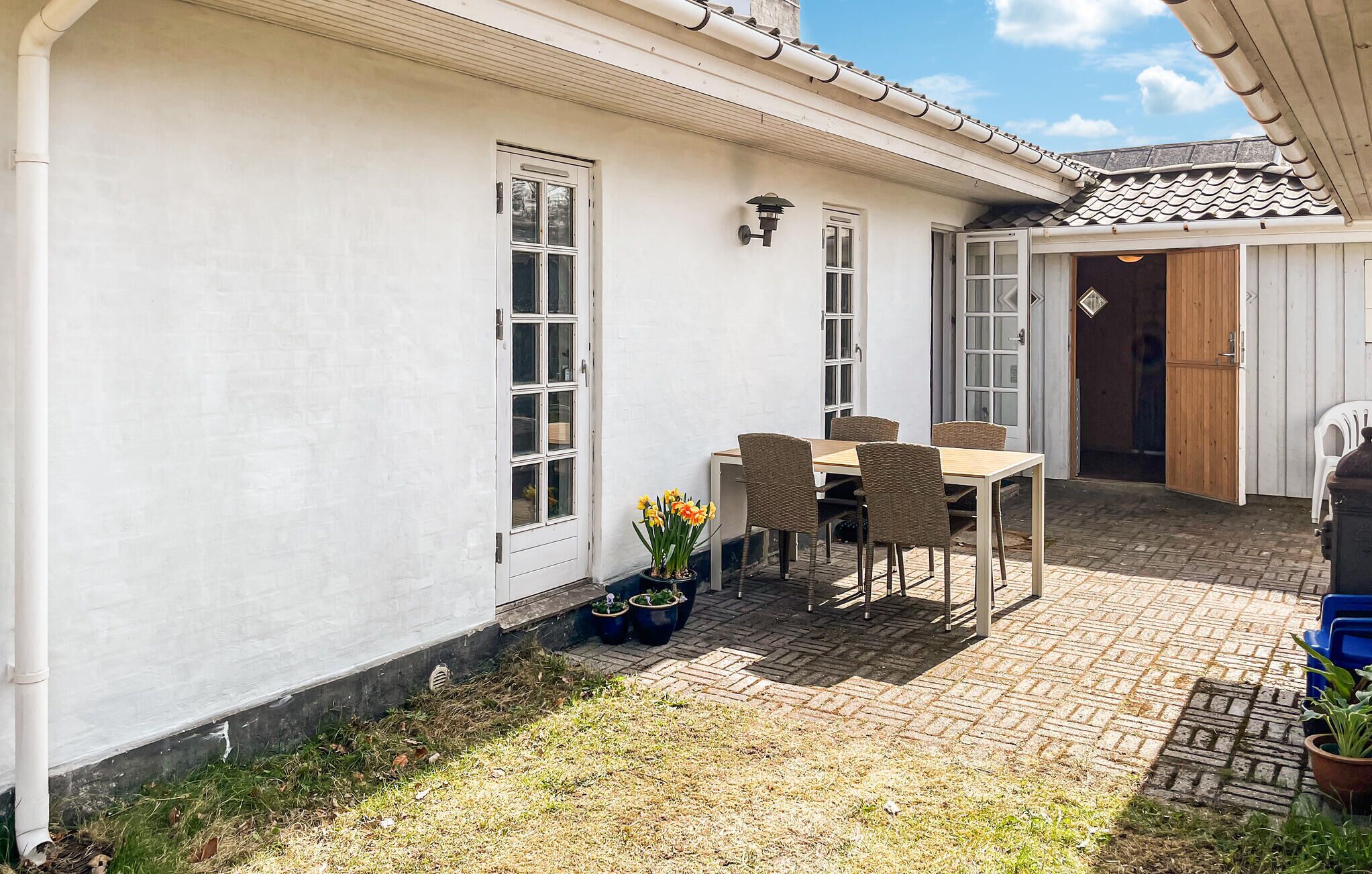 A white building with a tiled roof, a wooden door, and a table with chairs outside.