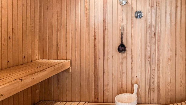 A sauna room with wooden walls, a wooden bench, a bucket, and a thermometer. - Amazing home in Hals with sauna (Hals)